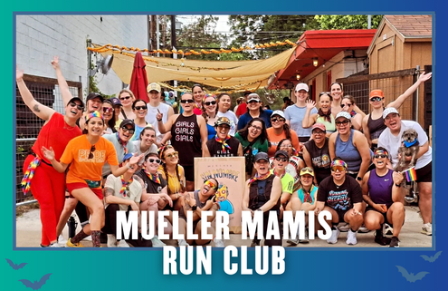 A diverse group of smiling women pose together outdoors, some wearing rainbow accessories and athletic gear, holding a sign that reads “Mueller Mamis Run Club.” Two small dogs are also present, celebrating the kickoff week of their marathon club with this joyful group run. Austin Marathon Half Marathon & 5K