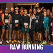 A group of runners in athletic gear pose together and smile at night on a city street under the text “RAW RUNNING.” Representing Latinas Run ATX, some wear hats and race bibs; a few flash peace signs, celebrating the spirit of a vibrant group run. Austin Marathon Half Marathon & 5K