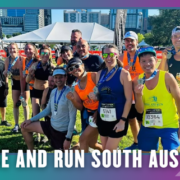 A diverse group of runners poses outdoors with medals, smiling after a Group Run. Tall city buildings and a white event tent are in the background. Text at the bottom reads: “RISE AND RUN SOUTH AUSTIN.”. Austin Marathon Half Marathon & 5K