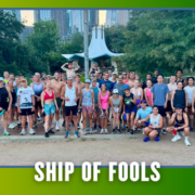 A large group of people in athletic wear poses outdoors in front of trees and a city skyline, representing the Cafecito Run Club during their KickOff Week. The text “SHIP OF FOOLS” appears at the bottom of the image, with bat graphics in the corners, highlighting the excitement of this special Group Run. Austin Marathon Half Marathon & 5K