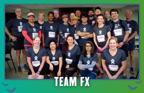 A group of people in matching “TEAM FX” shirts pose indoors, smiling after a Group Run during KickOff Week. They wear race bibs and medals, celebrating their achievement with Goodpain Athletics. The image has a green and blue border with “TEAM FX” written at the bottom. Austin Marathon Half Marathon & 5K