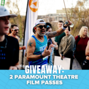 A group of runners at an outdoor event, with one man in sunglasses and a blue tank top cheering. Text on a blue banner reads: “GIVEAWAY: Win tickets—2 Paramount Theatre Film Passes.”. Austin Marathon Half Marathon & 5K