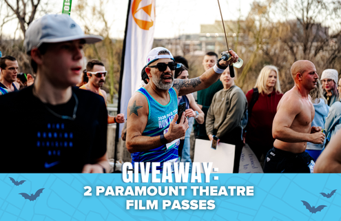 A group of runners at an outdoor event, with one man in sunglasses and a blue tank top cheering. Text on a blue banner reads: “GIVEAWAY: Win tickets—2 Paramount Theatre Film Passes.”. Austin Marathon Half Marathon & 5K