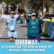 Two runners in blue shirts cheer as they approach the finish line of a race, capturing a moment perfect for a Finisher Pix photo package. A banner at the bottom reads, “GIVEAWAY: 8 CHANCES TO WIN A PAIR OF SHOKZ HEADPHONES.”. Austin Marathon Half Marathon & 5K