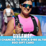 A smiling runner in pink gives a thumbs-up at a race. Text at the bottom reads: “GIVEAWAY: 3 chances to win a $150 Alter Ego gift card and Shokz Headphones,” with a blue background and bat graphics. Austin Marathon Half Marathon & 5K