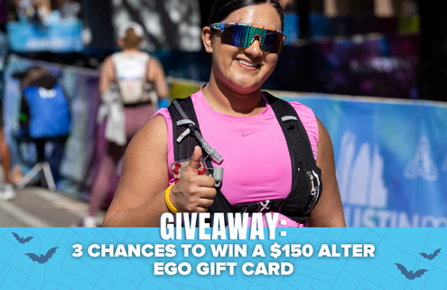 A smiling runner in pink gives a thumbs-up at a race. Text at the bottom reads: “GIVEAWAY: 3 chances to win a $150 Alter Ego gift card and Shokz Headphones,” with a blue background and bat graphics. Austin Marathon Half Marathon & 5K